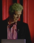 Small picture of David Byrne behind a lectern.  Looking down.