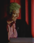 Small picture of David Byrne behind a lectern, laughing to himself.